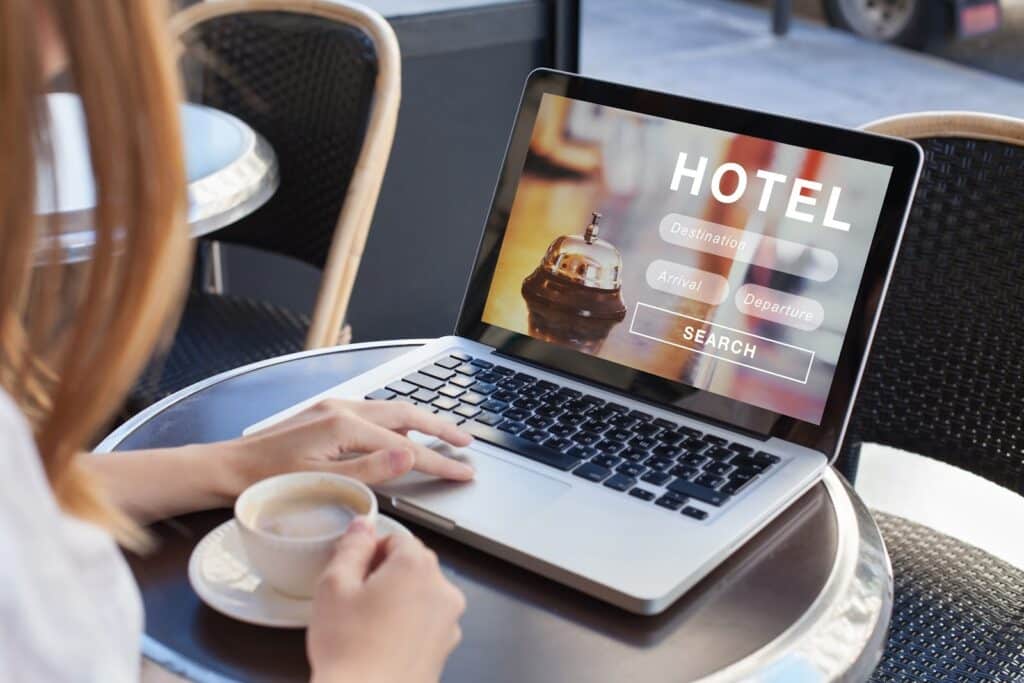 Woman browsing a hotel search interface on a laptop while holding a coffee, representing personalised retargeting strategies to re-engage potential guests